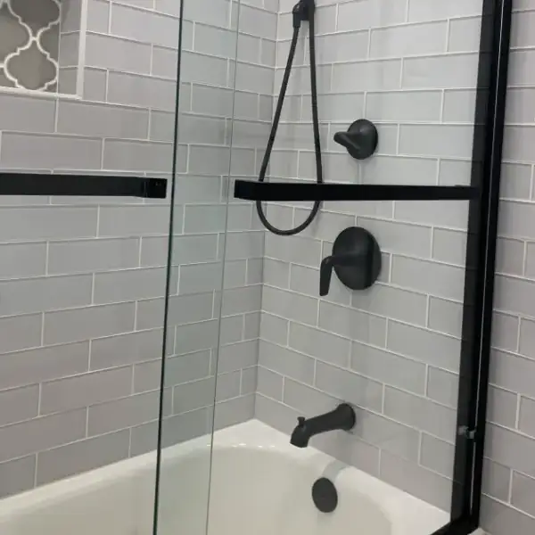Modern bathroom with glass door and black fixtures.