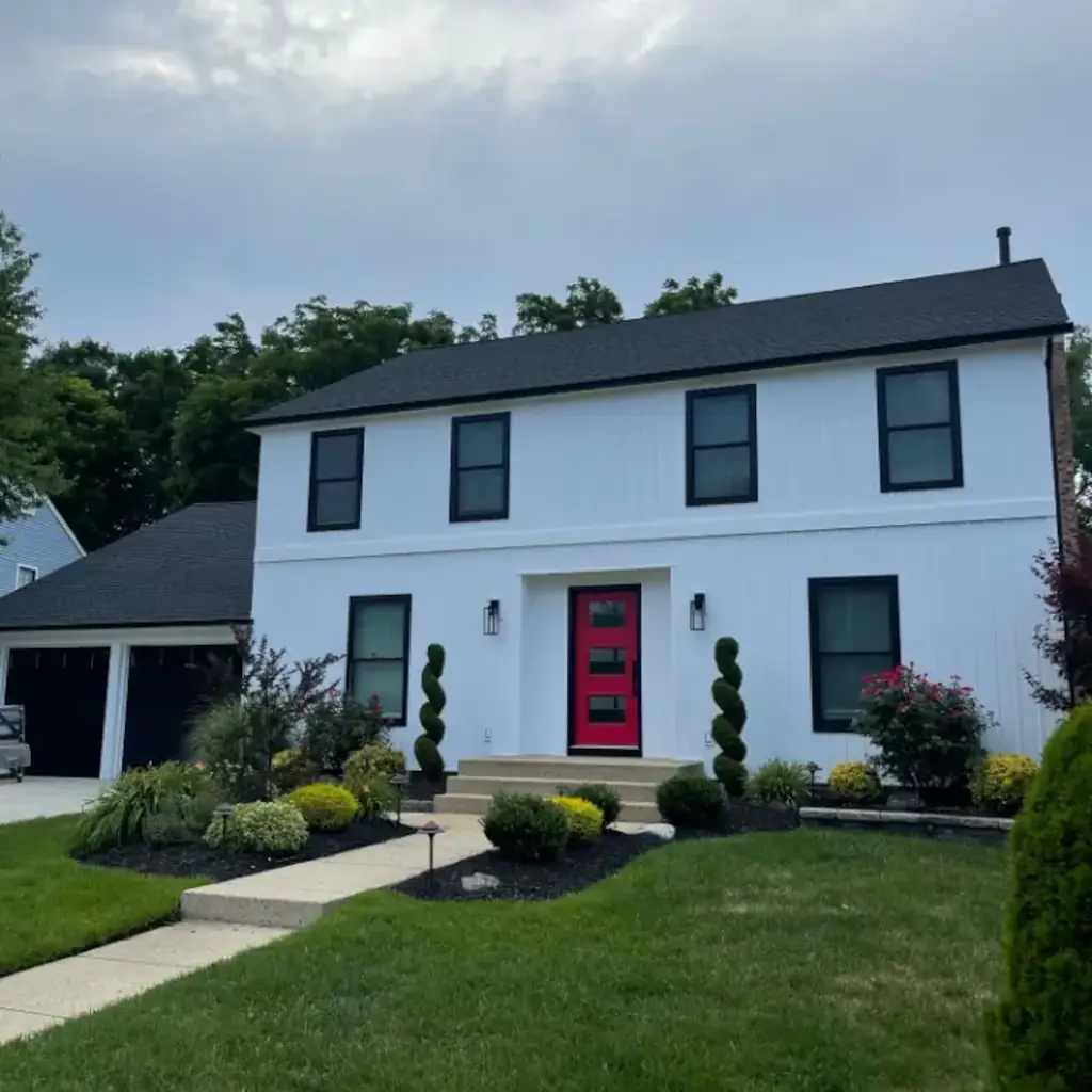 A white home with red door and greenery.