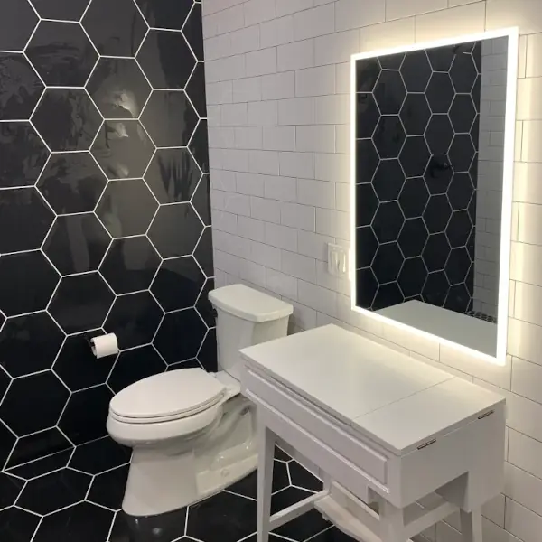 Modern bathroom with black hexagonal tile accent wall, white toilet, white vanity, and an illuminated rectangular mirror.